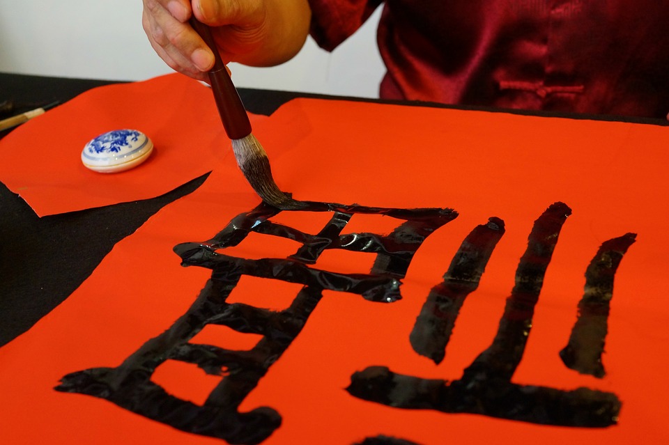 pessoa escrevendo ideograma chinês com um pincel sobre um papel vermelho