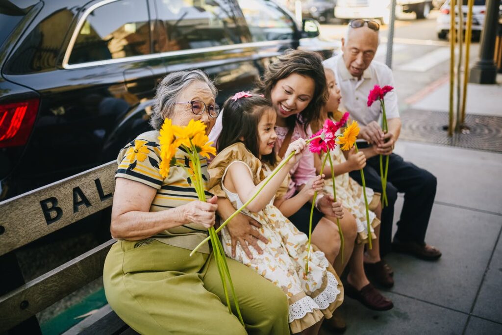 um casal de idosos sorridentes sentados felizes com o restante da familia em um banco e segurando flores 