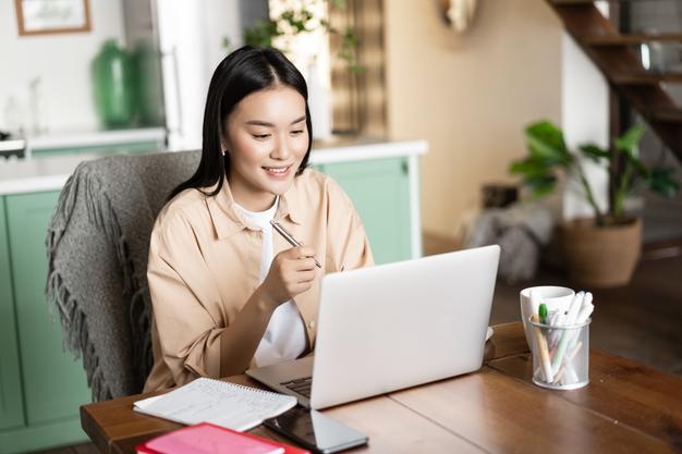 menina asiática sorridente estudando em casa em frente a um laptop