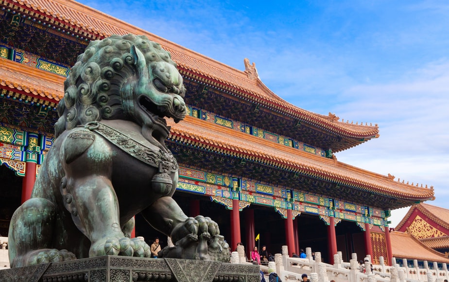 um grande templo chines ao fundo com uma estatua em primeiro plano