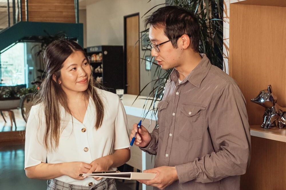 Aprender mandarim para negócios, estabelecendo um ambiente de negócios mais colaborativo e respeitoso. Na foto temos dois colegas de trabalho conversando.